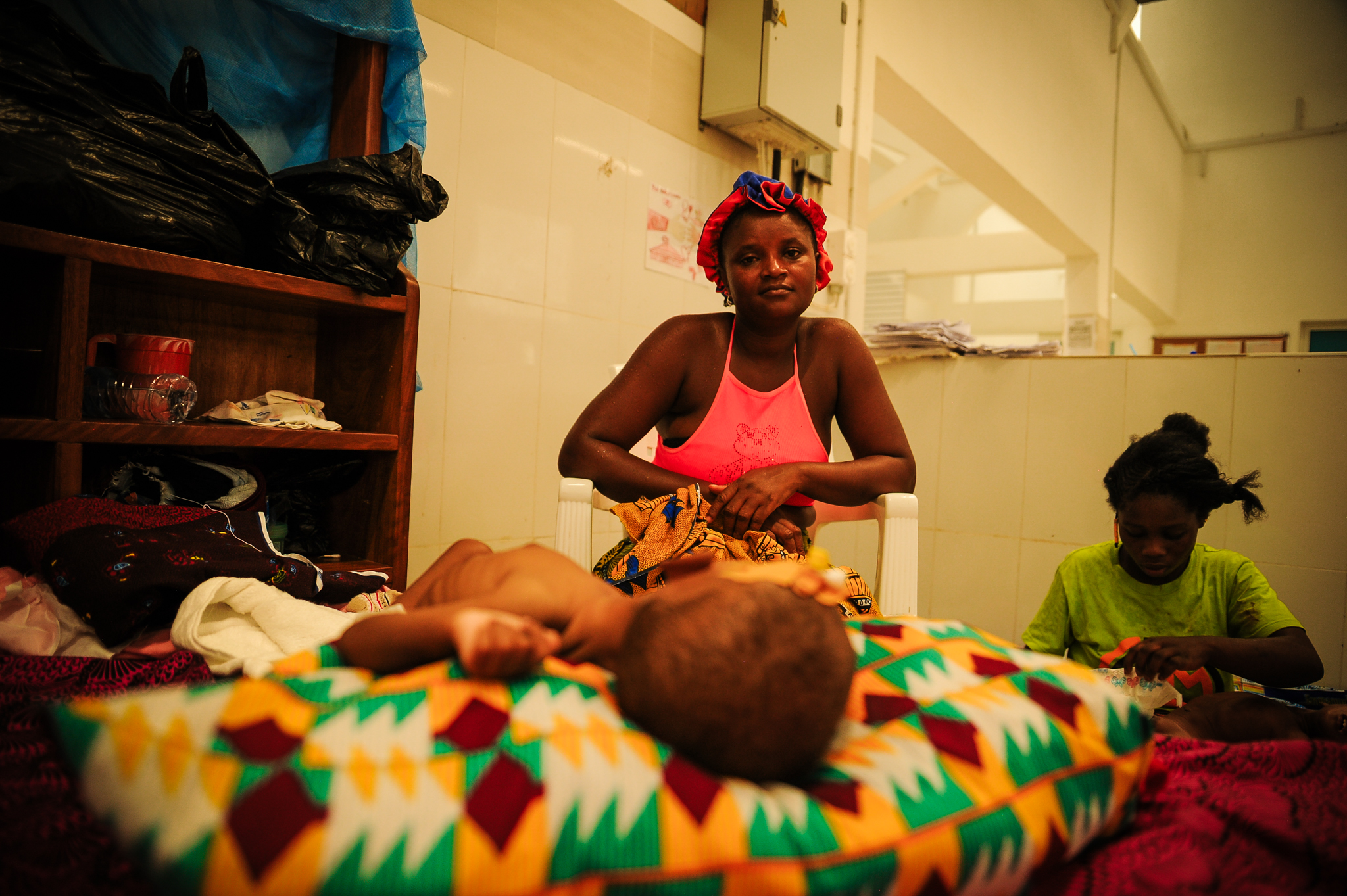 A mother sits with her child on an inpatient bed at the Jesus Loves Me Children's Center
