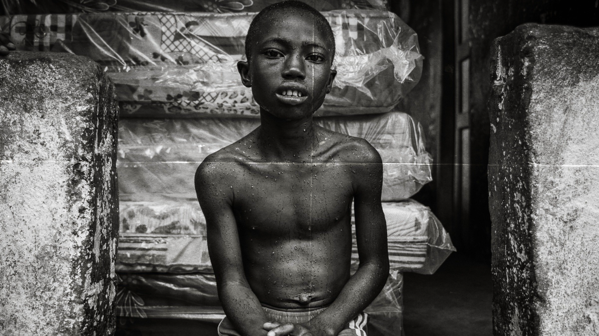 A boy sits upright, drenched in the sweat of a malaria fever