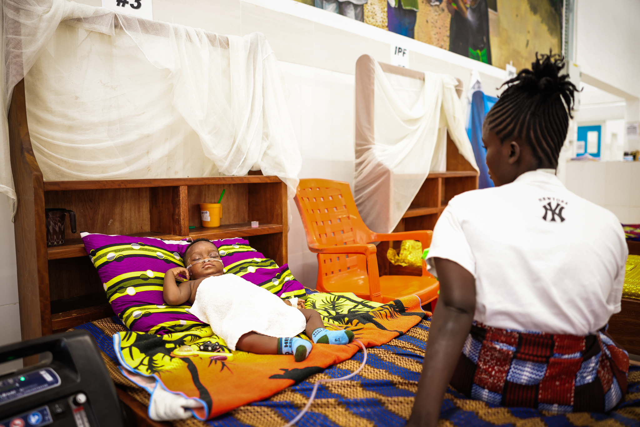 A child rests on oxygen in numbered bed 3 while their mother sits alongside