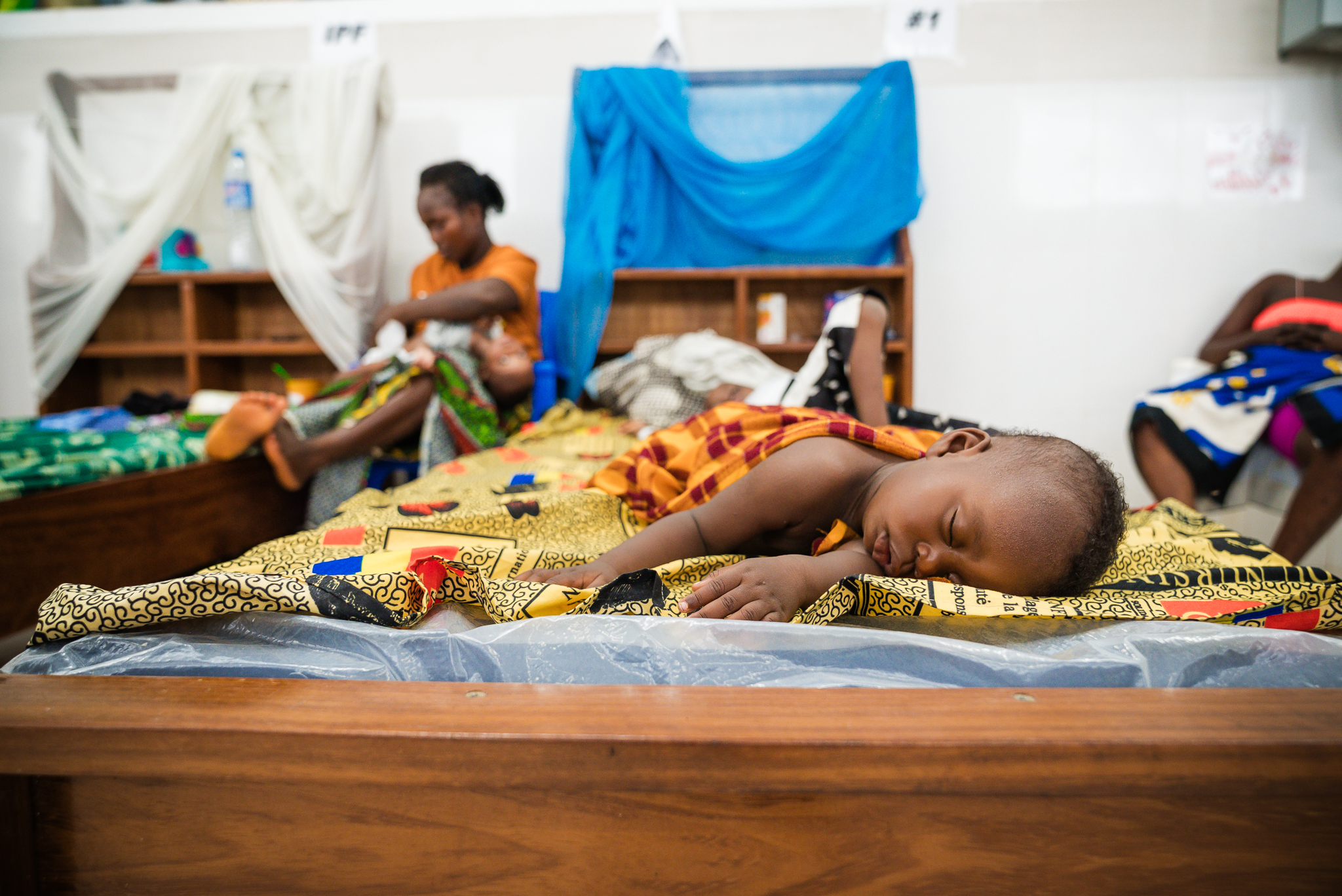 A child sleeps in an inpatient bed at the Jesus Loves Me Children's Center, with the ward behind