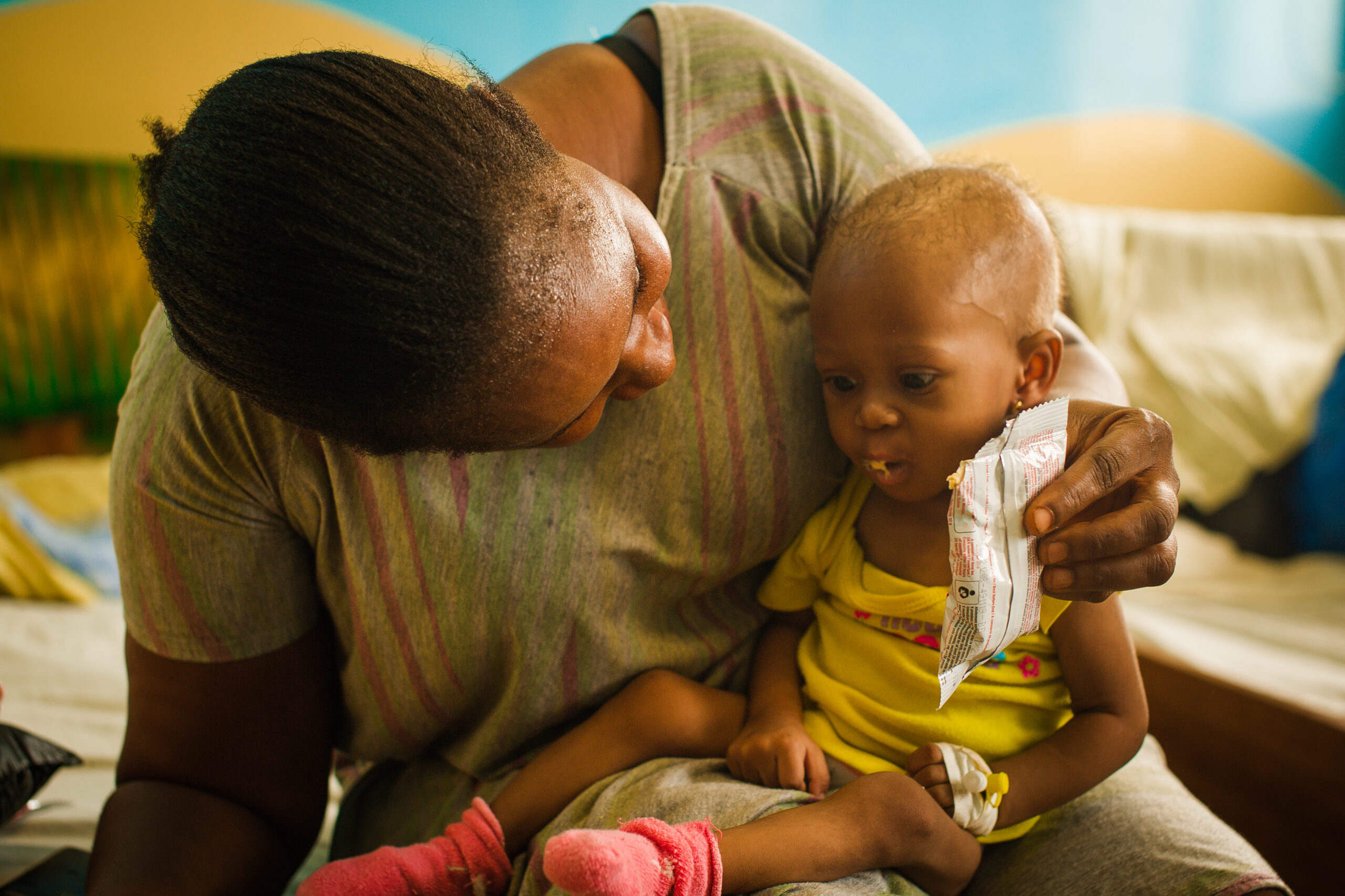 A caretaker feeds a recovering child from a sachet of therapeutic food