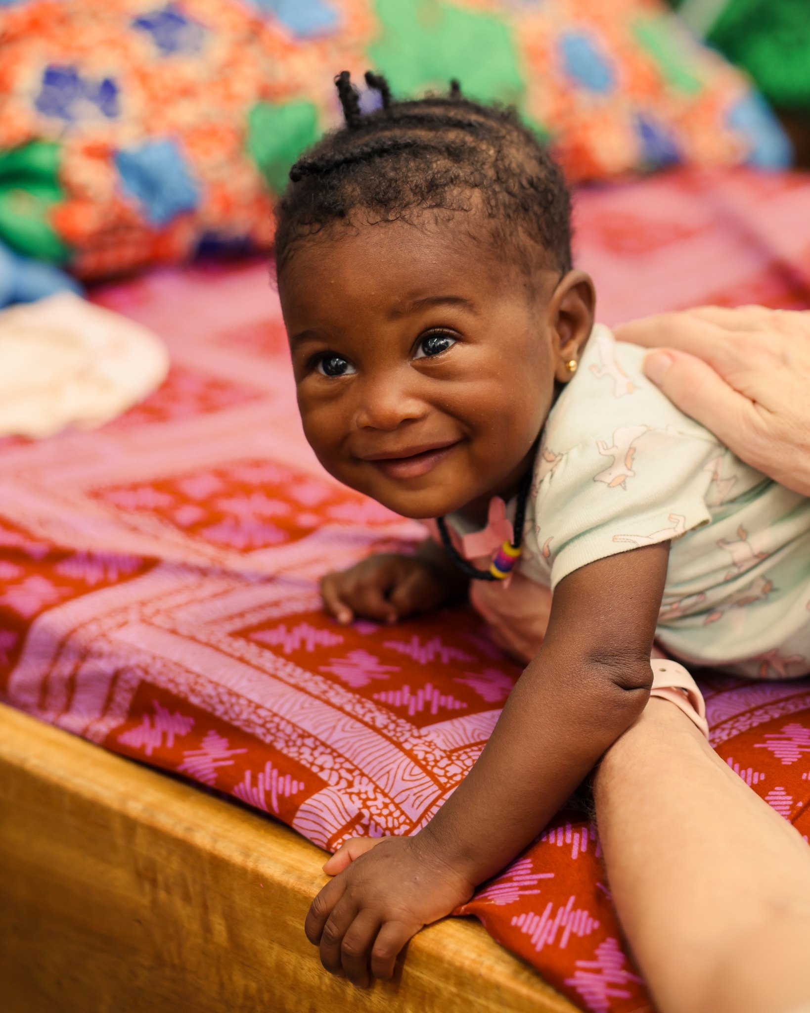 A smiling baby on a ward bed at the Jesus Loves Me Children's Center.