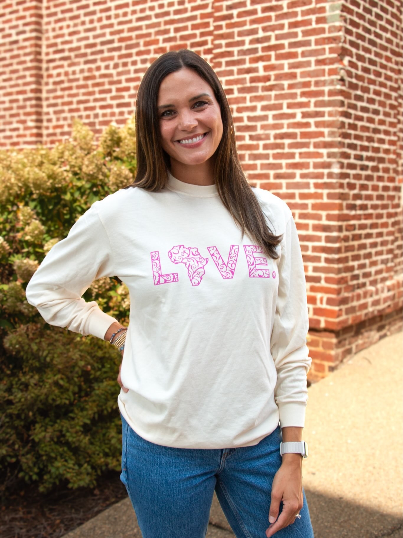 A woman smiles in a cream LOVE. sweatshirt.