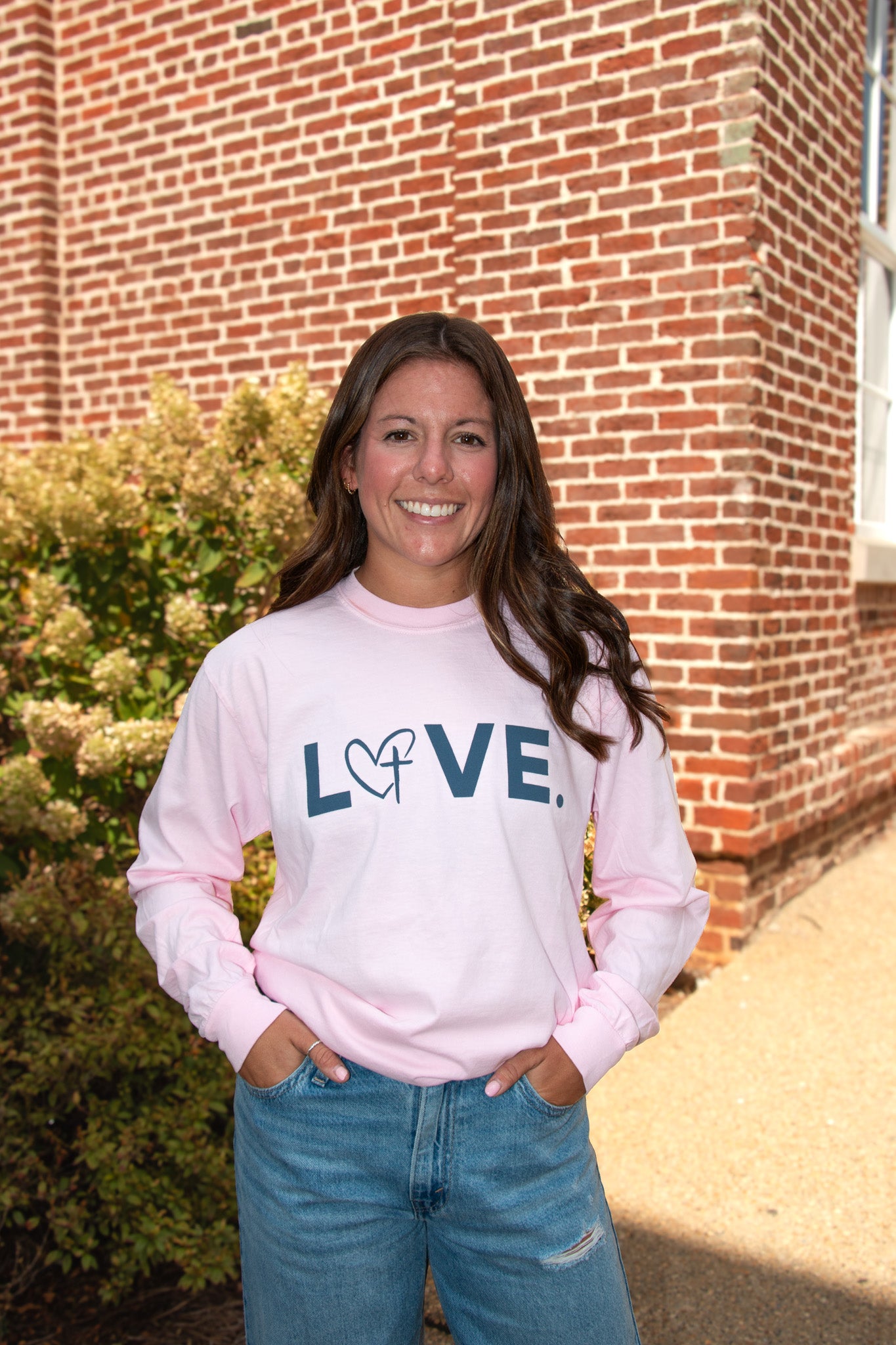 A woman wears a blossom pink LOVE. long sleeve tee outside The LOVE. Store.
